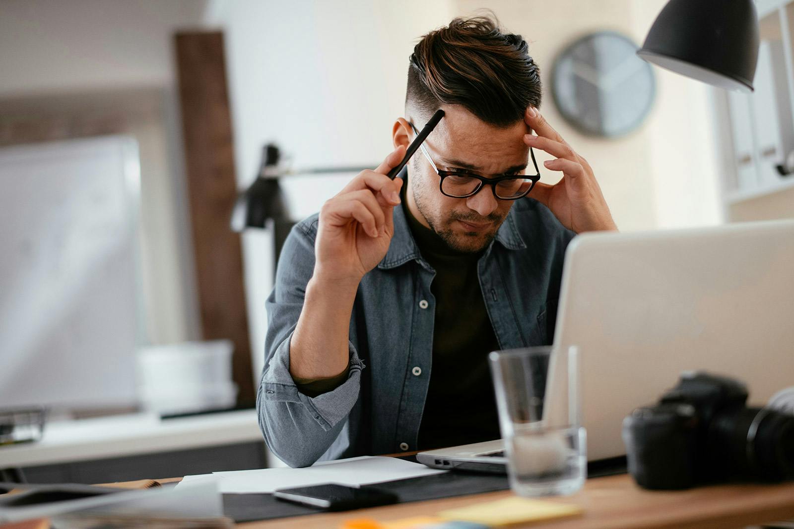 man with glasses in front of the computer deep in thought