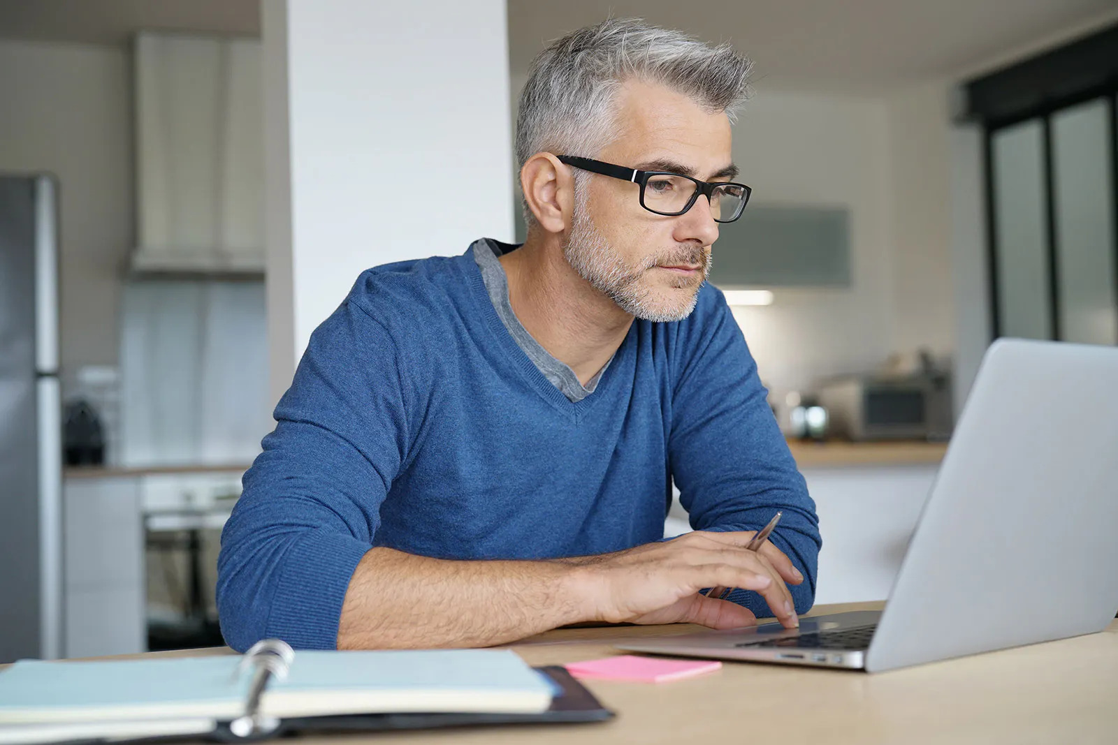 An elderly man works remotely on his laptop.