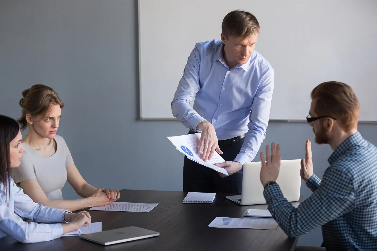 In a conference room, a supervisor waves papers while talking to an intimidated employee.